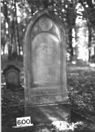 Grabstein 600 (Index: 99900699) Material: Sandstein Zustand: stark verwittert Maße HxBxT: 142x52x19 cm Beschreibung: aufgesockelte Stele mit Spitzbogenabschluss, Schriftfeld oben umrahmt von Maßwerk, im Medaillon im Bogenfeld Blüte Symbolik: Blüte: Grabstein 600