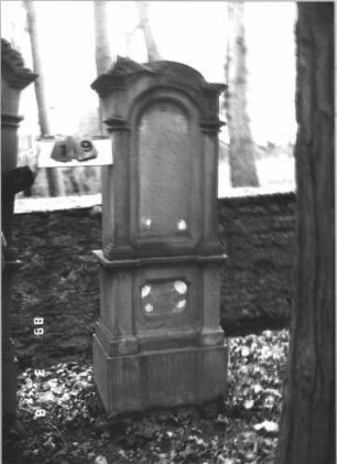 Grabstein 19 (Index: 99808666) Material: Sandstein Zustand: Giebel beschädigt, Schrifttafeln fehlten Maße HxBxT: 179x62x37 cm Beschreibung: Ädikula, flankiert von 2 Halbsäulen, mehrfach gegliederter Sockel, Abschluß zerstört, eingesetzte Schrifttafeln (fehlen) Besonderheit: Foto unscharf: Grabstein 19