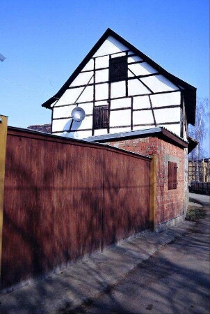 Plankenzaun; anschließend Flachdach-Gebäude; Fachwerkgiebel