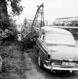 B 206: Mönkhagen-Langniendorf: Verkehrsunfall eines Reisebusses mit einem Pkw: verunglückter Pkw an Seil eines Abschleppwagens: links zwei Arbeiter: daneben Baum: hinten rechts Bus