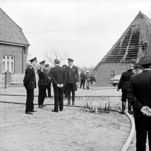 Großensee: Amtsfeuerwehrfest des Amtes Lütjensee: Brandübung: links Wehrführer bei der Begutachtung: am Boden ausgerollte Feuerwehrschläuche, Schlauchtrommel: hinten Feuerwehrmänner beim Löschen, hinten rechts baufällige Scheune mit Reetdach: im Vordergrund rechts Feuerwehrmann [Rückenansicht]