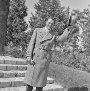 Mann in Hut und Mantel im Park vor einem Denkmal