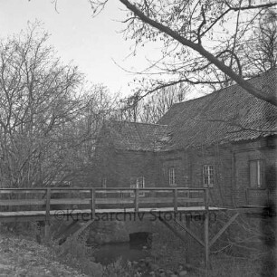 Denkmal: Kupfermühle mit beschädigtem Dach und in desolatem Zustand: vorn beschädigte Holzbrücke über Glinder Au: hinten Bäume