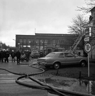 Brand: Gies Kerzen GmbH: Möllner Landstraße: Feuer in Parafinturm: vorn Wasserschläuche: rechts dahinter Pkw und Löschfahrzeug mit Leiter: darauf Feuerwehrmann: hinten weitere Löschfahrzeuge und Feuerwehrleute: im Hintergrund Gewerbehalle