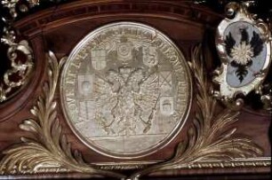 Türbekrönung mit einem Medaillon, welches den kaiserlichen Doppeladler umgeben von den Wappen der sieben Kurfürsten zeigt, seitlich Putten mit Wappen und Krone des Heiligen Römischen Reichs