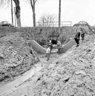 Norderbeste: Flussregulierung: Ausbau des Bachzuflusses: hinten Mitte und rechts Arbeiter mit Schaufeln beim Bau der Sohlgleite: vorn rechts und links Erdhaufen: im Hintergrund Brücke der Bundesstraße B 75 mit Geländer und Bäumen: hinten rechts und links VW-Käfer