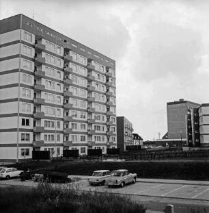 Schanzenbarg: vorn unbefestigtes Gelände, Straße und Parkplatz mit parkenden Pkws: links dahinter mehrgeschossiges Hochhaus: rechts dahinter unbefestigtes Gelände: hinten rechts zwei viergeschossige Wohnblocks und Wohnhaus: 20. Juni 1968