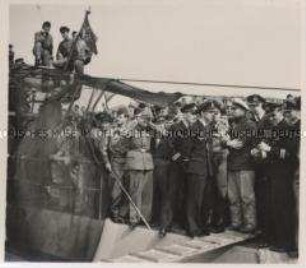Wehrmachtssoldaten, U-Boot, Kameraden der Kriegsmarine des Heeres und der Luftwaffe, sowie Arbeiter der Werft begrüßen das mit Siegeswimpeln zurückgekehrte Boot an der Pier. Der Kommandant erzählt den Kameraden von der Unternehmung.