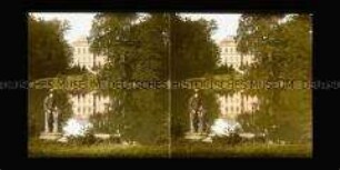 Parkanlage mit Teich, im Vordergrund sitzender Junge,im Hintergrund Schloss