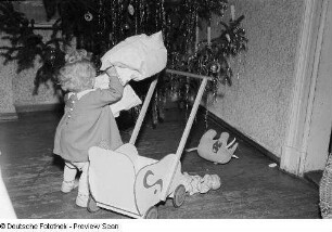 Porträt eines kleinen Mädchens mit Puppenwagen vor einem Weihnachtsbaum