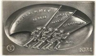 Jahresplakette (dargestellt: Drei Werkleute stoßen mit Gewalt drei Fahnen im Gegenwind vorwärts) : Idee: Einigkeit und Recht und Freiheit