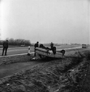 B 75: Höhe Gewerbegebiet zwischen Bad Oldesloe und Blumendorf: Verkehrsunfall: PKw von Fahrbahn abgekommen: Unfallwagen liegt auf Dach, daneben Fahrer [Rückenansicht], auf Fahrradweg: links Straße: an Straßenrand zwei Polizisten: Leitpfosten: hinten Kleintransporter: Reifglätte
