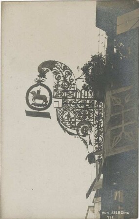 Sterzing (Südtirol, Italien): Nasenschild, Schmiedeeisen, mit Lamm Gottes: an Fassade von Fachwerkhaus: unten handschriftliche Notiz;