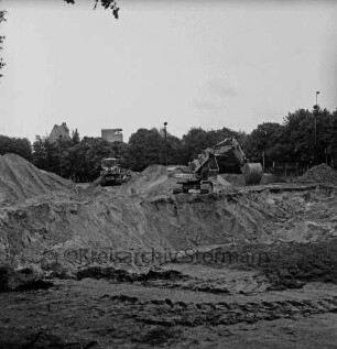 Konrad-Adenauer-Ring: Bauarbeiten für Unterführung am Exer: zwei Bagger auf Erdhaufen: hinten links hinter Bäumen Gebäude der Weizenmühle ("Gloria-Mühle") der Johannes Ströh Mühlenwerke