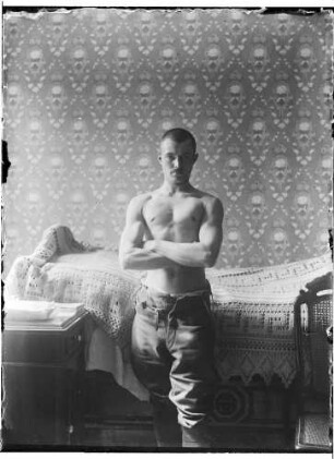Wolfgang Knochenhauer, stehend mit freiem Oberkörper vor einem Bett posierend