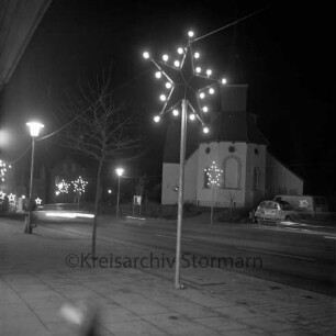 Paul-von-Schoenaich-Straße: Nachtaufnahme: Weihnachtsbeleuchtung: auf Gehwegen Lichtersterne, Straßenlampe, Baum: rechts Matthias-Claudius-Kirche, parkende Autos