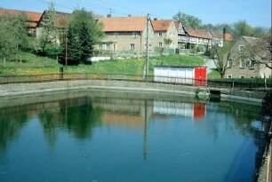 Feuerlöschteich mit Betonmauer und Lattenzaun, umliegende Häuser