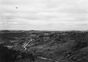 Landschaftsblick : Blick in eine hügelige Landschaft mit vereinzelten Häusern an einer Straße in der Bildmitte.