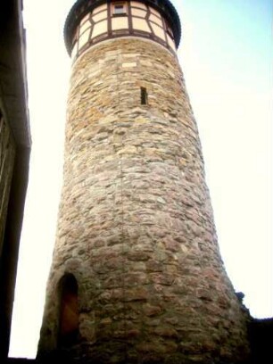 Nordwestlicher Eckturm (Hutsturm) aus dem Kirchhof mit Schießscharte sowie Werksteinen im Mauersteinverband und Fachwerk-Turmabschluß