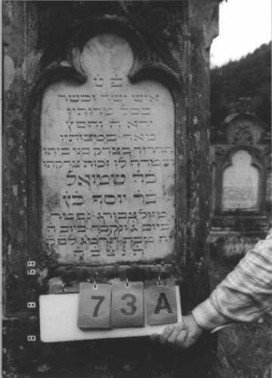 Grabstein 73 (Index: 99799553) Material: Sandstein, Schriftplatte Marmor Zustand: verwittert Maße HxBxT: 178x64x27 cm Beschreibung: Stele, Abschluß mit Mittelerhöhung, Sattelverdachung, Zinnenaufsatz, eingelassene Schriftplatte mit Kleeblattbogenabschluß, getreppter Sockel Symbolik: floral: Grabstein 73A