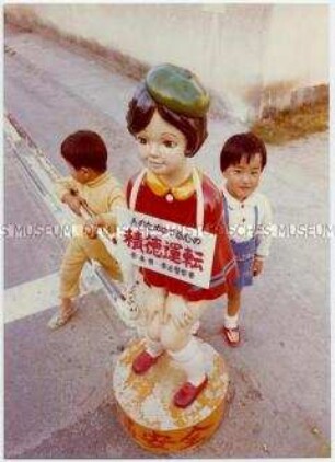 Zwei japanische Kinder neben einer bunten Figur am Straßenrand