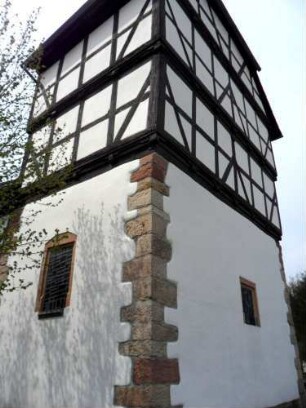 Evangelische Kirche - Kirchturm von Südosten mit zwei Fachwerk-Geschossen über steinernem Erdgeschoß mit sichtiger Eckquaderung (Chorraum)