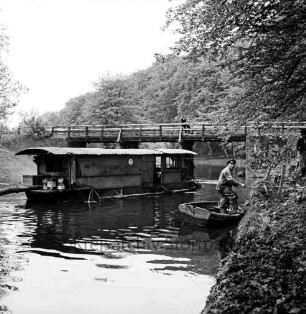 Trave: Entschlammungsarbeiten: Schwimmbagger mit Saugrohren: vorn rechts Ruderboot mit Arbeiter: hinten Friedensbrücke: darauf Zuschauer: im Hintergrund Wald