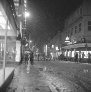 Mühlenstraße: verkaufsoffener Sonnabend mit Fußgängerzone: rechts Einmündung Hindenburgstraße: rechts und links Wohn- und Geschäftshäuser: dazwischen Fußgänger: vorn links Schaufenster des Kaufhauses Nickel: Winter: Abend: 8. Dezember 1973