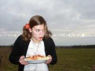 Junge Frau Spaghetti essend auf einem Feld (Altersgruppe 18-21)