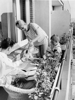 Familie Keller befindet sich auf ihrem Balkon in der Königstraße. Sie gießt Saft in ein Glas. Auf dem Tisch befindet sich eine Schüssel mit Obst - Ausdruck gesunder Lebensweise. Werbefotografie für die Techniker Krankenkasse (TK)