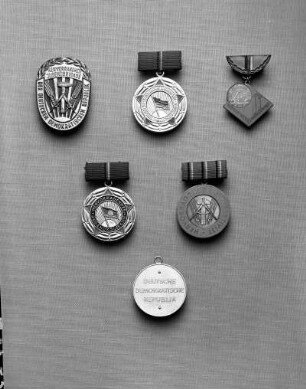 Ehrentitel der Deutschen Demokratischen Republik (DDR). Oben: Ehrenzeichen "Hervorragende Jugendbrigade der DDR" (1956/1963 verliehen). Erste Form (Bronze, blau emailliert; 40 x 30 mm; 1956/1957 verliehen); zweite Form, Variante mit Deutschlandfahne (silberfarben, hellblau emailliert; 30 mm Durchmesser; 1958/1959 verliehen) an Spange (hellblau bezogen; 11 x 24 mm); Medaille "Hervorragender Jungaktivist". Erste Form (blau emailliert; 21 x 29 mm; 1960/1962 verliehen) an halbkreisförmiger Spange (emailliert). Mitte: Medaille "Hervorragendes Jugendkollektiv der DDR" (versilbert, hellblau emailliert; 30 mm Durchmesser; ab 1964 verliehen) an Spange (blau bezogen; 12 x 24 mm); Medaille "Hervorragender Jungaktivist", Zweite Form (versilbert, geprägt; 30 mm Durchmesser; ab 1963 verliehen) an Spange (hellblau bezogen; 11 x 25 mm). Unten: Rückseite zur Medaille "Hervorragender Jungaktivist", zweite Form