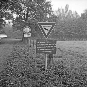 Nienwohlder Moor: Naturschutzgebiet: Hinweisschild sowie Straßenschild: links Straße und hinten Pkw: rechts Moorwiese: im Hintergrund Bäume und Sträucher