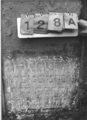 Grabstein 128 (Index: 99608812) Material: Sandstein Zustand: sehr stark verwittert mit großem Textverlust Maße HxBxT: 103x72x11 cm Beschreibung: Stele mit geschwungenem Rundbogen, vertiefter Textteil mit Rundbogen: Grabstein 128A
