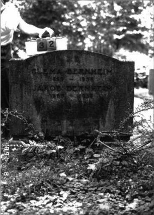 Grabstein 32 (Index: 100102098) Material: Kalkstein, aufgesetzte Metallbuchstaben Zustand: gut Maße HxBxT: 100x102x26 cm Beschreibung: Stele, breit, profilierter Sockel, eingezogener Segmentbogenabschluß Besonderheit: Doppelgrab: Grabstein 32