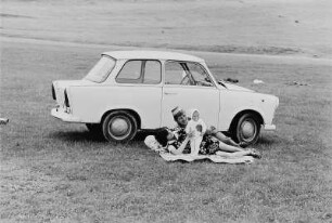 Junge Familie mit PKW "Trabant" auf einer Wiese