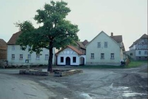 weiträumiger Dorfplatz mit Baum, der von einer Mauer gefasst ist