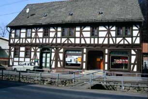 denkmalgeschütztes Fachwerkhaus, früher Konsum, jetzt Fleischerei; davor Bachlauf mit Brücke
