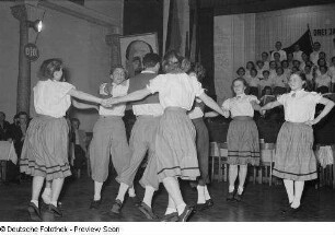 Tänzer in Tracht der Leipziger Eisen- und Stahlwerke, im Hintergrund ein Chor sowie ein Porträt Walter Ulbrichts