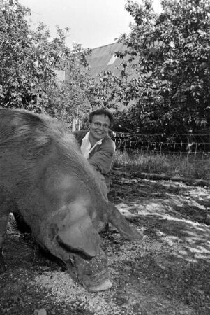Hof von Günther Fielmann: Besitzer hockend bei der Fütterung von Schwein Borsti: im Hintergrund Scheune