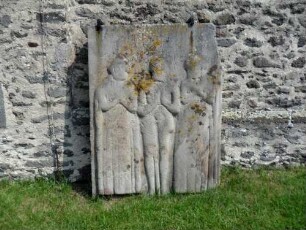 Kirchturm von Süden im Südsüdwesten - Grabsteinfragment aus dem (aufgelösten) Kirchhof mit Personendarstellung in Hochrelief-Manier (verwittert)