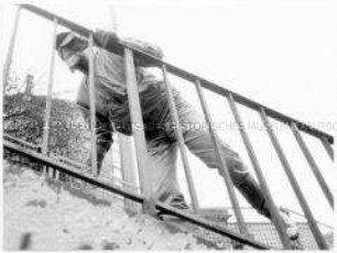Vermummte Gestalt hinter einem Treppengeländer, von unten fotografiert (Altersgruppe 18-21)