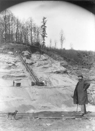Abbau von Sand/Kies am Hang einer bewaldeten Kuppe. Förderung der Massen per Rutsche zur Ladestelle der Feldbahn-Muldenkipploren. Im Vordergrund Herr (wohl Grubenbesitzer) mit Hund : Abbau von Sand/Kies am Hang einer bewaldeten Kuppe. Förderung der Massen per Rutsche zur Ladestelle der Feldbahn-Muldenkipploren. Im Vordergrund Herr (wohl Grubenbesitzer) mit Hund