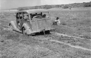 Auto im Schlamm : Mann, der neben einem im Schlamm steckengebliebenen Fahrzeug sitzt