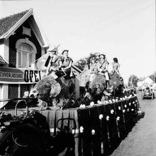 Karpfenfest: Umzug: Festwagen, Fischerinnen reiten auf mehreren Riesenkarpfen, gezogen von Traktor: im Hintergrund weiterer Festwagen: links Hausfassade mit Transparent, 11. Oktober 1959