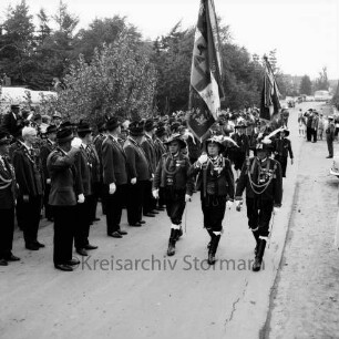 Schützenfest, 10-jähriges Jubiläum: Veranstalter Schützenverein Reinfeld und Umgebung von 1954 e.V.: zugleich Pokalschießen des Kreisschützenverbands Stormarn: Umzug: Elschenbek: links Schützenplatz: auf Straße Fahnenabordnung der Tiroler Schützen der Schützenkompanie Wilten (bei Innsbruck), schreitet Front der angetretenen Schützen ab: hinten Zuschauer, parkende Autos, 6. September 1964