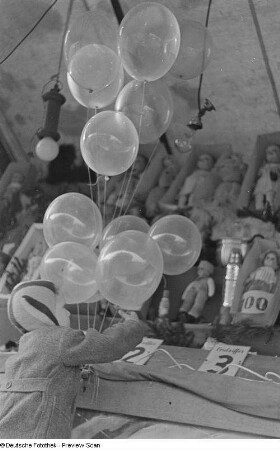Kind an einem Losstand nach Luftballons greifend