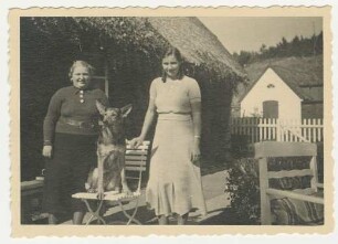 Frau und junge Frau: dazwischen auf Gartenstuhl Schäferhund: Rohlfshagen, Kupfermühle, in Garten von Wohnhaus Schäferkate: dahinter links Traufseite Wohnhaus, hinten Gartenzaun, vorne rechts Gartenstuhl: hinten rechts Atelier: im Hintergrund Wiese an Abhang