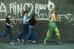 Aufnahme für die Reportagereihe „Außenseiter der Mode“: Studio Fong Leng, Amsterdam : Model in gelbem Top und grünen Pluderhosen nach Entwürfen von Fong Leng, mit einem Basketball und drei Jungs vor einer Graffitiwand