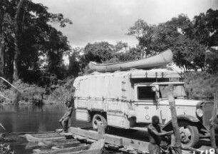 Automobil auf einem Floß : Ein Lkw der Schomburgk-Expedition wird von zwei Männern auf einem Floß über den Fluss gesetzt