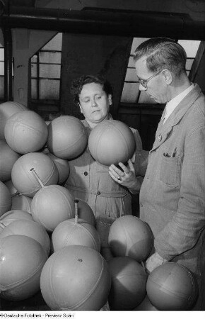 Zwei Personen in Arbeitsbekleidung begutachten Ballblasen[?]